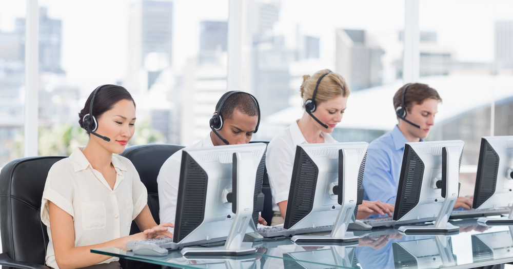 Group,Of,Business,Colleagues,With,Headsets,Using,Computers,At,Office